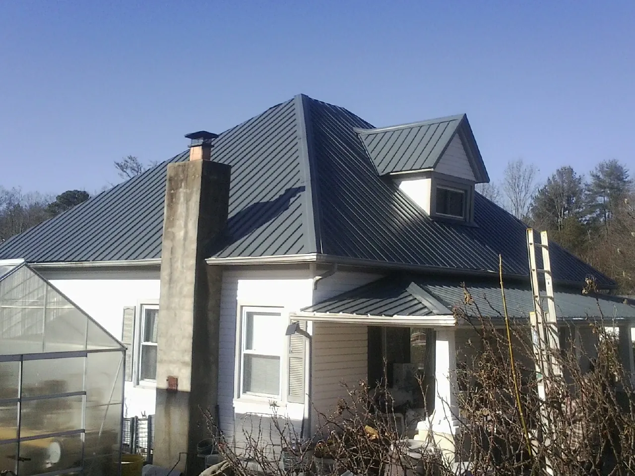 Dark blue standing seam metal roof on a white farmhouse with dormer — Slate & Tile Roof Repair by Roofing Brothers in Bay Center