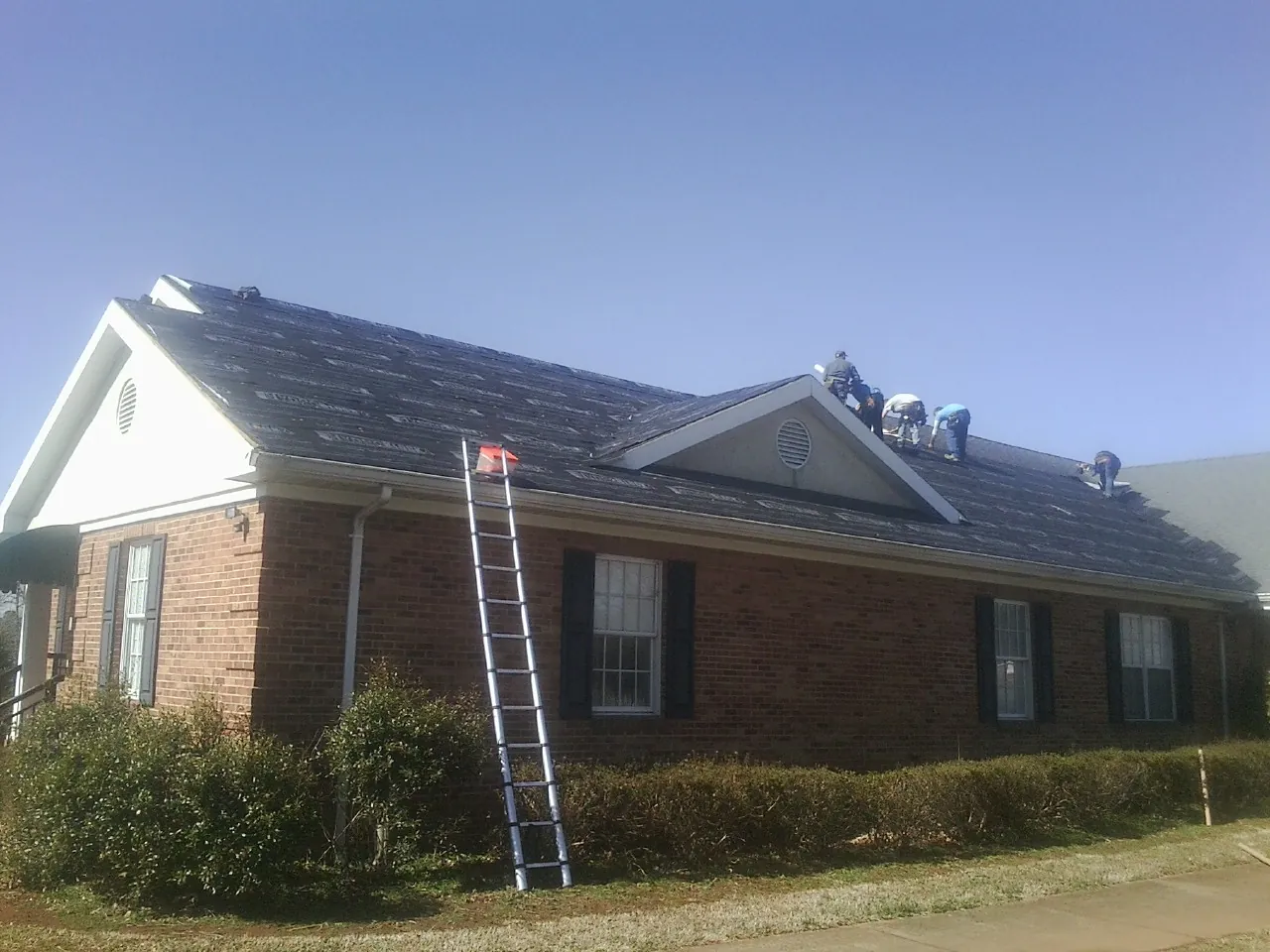 Crew tearing shingles off a brick ranch roof with a ladder set — Emergency Roof Repair work by our crew in Bay Center