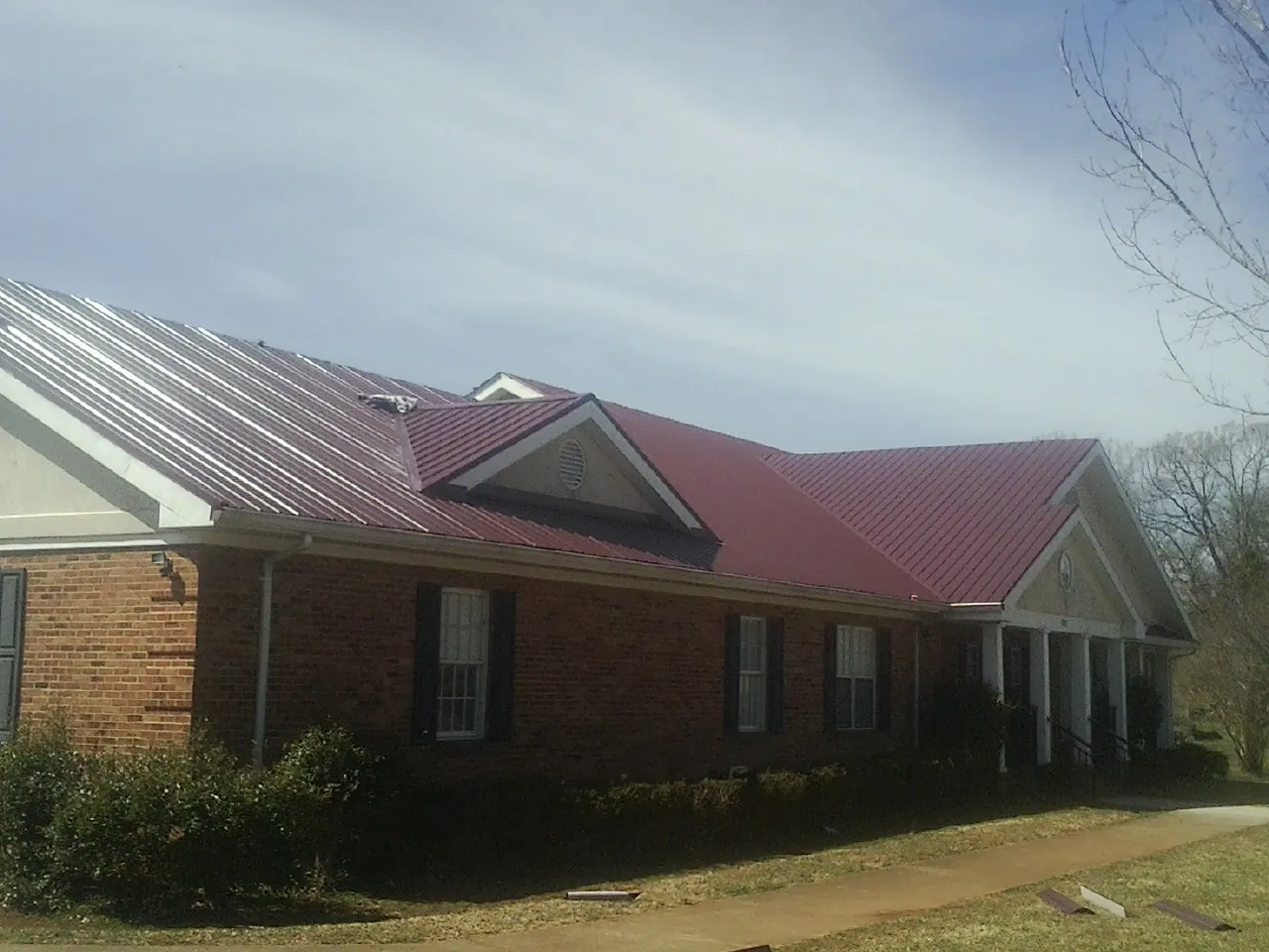 Red metal roof with gabled entries on a long brick building, from a Hail Damage Roof Repair job in Bay Center