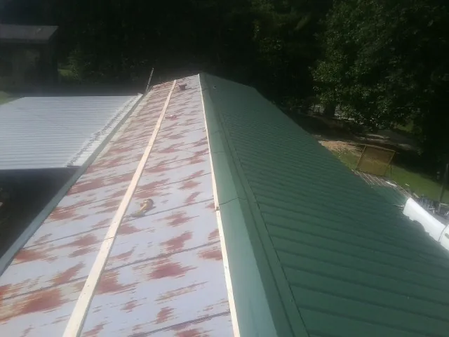 Old rusted panels beside newly installed green metal roofing — Wind Damage Roof Repair by Roofing Brothers in Bay Center