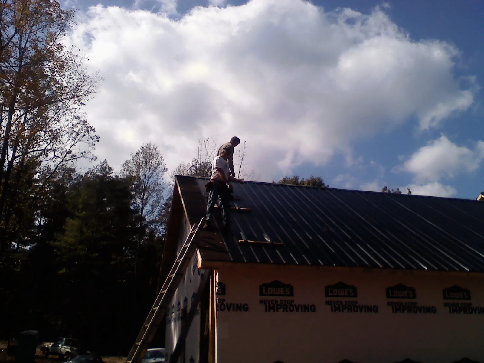Roofer fastening dark metal panels high against a cloudy sky, from a Roof Inspection job in Bay Center