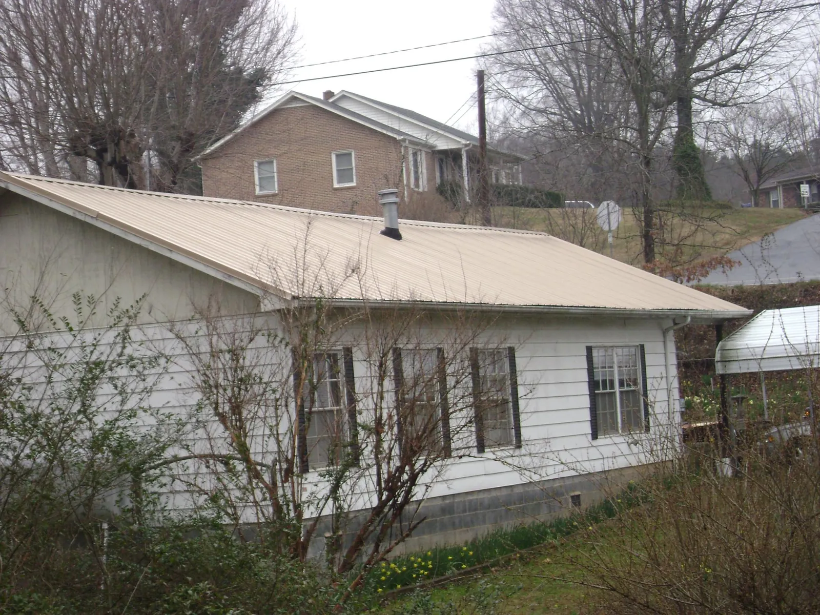 Tan metal roof on a white sided house set into a hillside — Commercial Roofing by Roofing Brothers in Bay Center