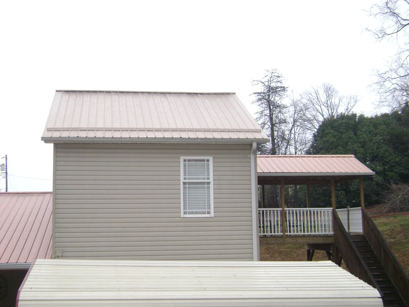 Tan metal roofs on a two story addition and attached porch, from a Roof Replacement job in Bay Center